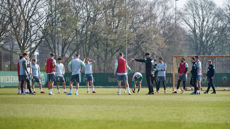 Werder-Coach Ole Werner erklärt während des Trainings seinen Spielern etwas, die im Kreis um ihn herum stehen.