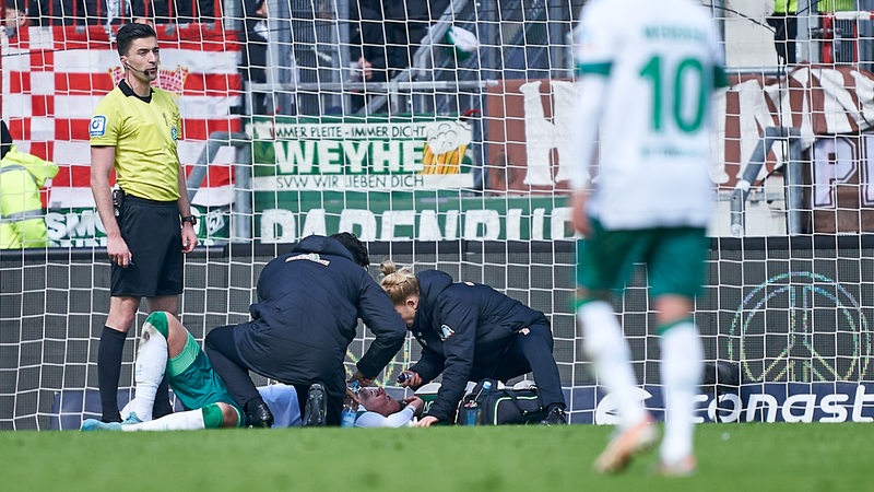 Werder-Spieler Marco Friedl wird auf dem Spielfeld nach einem Zusammenstoß behandelt.