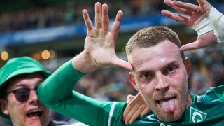 Werder-Stürmer Marvin Ducksch neben einem Fan mit seinem Markenzeichenjubel mit herausgestreckter Zunge.