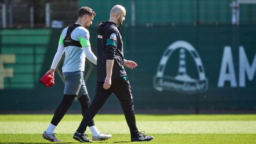 Werder-Verteidiger Milos Veljkovic verlässt mit einem Betreuer vorzeitig das Training.