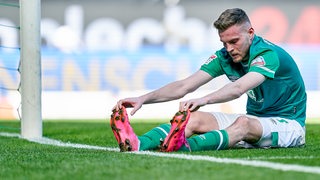 Werder-Stürmer Marvin Ducksch sitzt frustriert und breitbeinig nach einer verpassten Torchance auf dem Rasen.