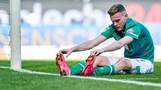 Werder-Stürmer Marvin Ducksch sitzt frustriert und breitbeinig nach einer verpassten Torchance auf dem Rasen.