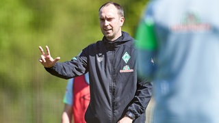 Werder-Coach Ole Werner zeigt lächelnd beim Training drei Finger hoch.