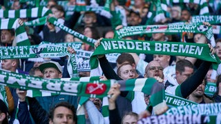 Blick auf dicht gedrängt stehende Werder-Fans im Stadion, die Schals hochhalten.