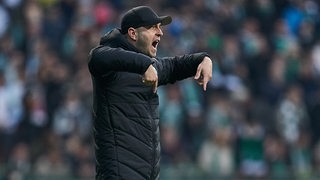 Werder-Trainer Ole Werner ruft über den Platz und zeigt mit den Fingern zu Boden.