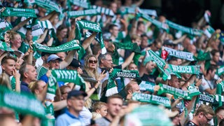 Werder-Fans stehen dicht gedrängt auf einer Tribüne und halten zahlreiche grün-weiße Schals hoch.