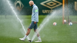 Werder-Kapitän Ömer Toprak läuft am Rande des Trainings gedankenverloren durch einen Rasensprenger.