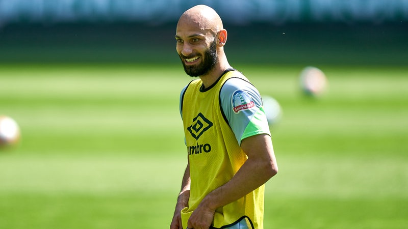 Werder-Kapitän Ömer Toprak mit gelbem Leibchen lächelt während des Trainings.