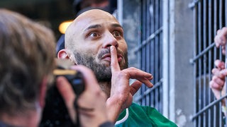 Werder-Kapitän Ömer Toprak steht vor dem Fan-Zaun und legt den Finger auf den Mund.