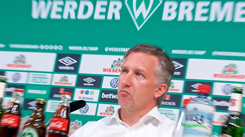Frank Baumann herangezoomt mit ernster Miene auf dem Podium einer Werder-Pressekonferenz.