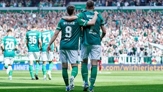 Die Werder-Spieler Mitchell Weiser und Marvin Ducksch schlendern Arm in Arm über den Platz.