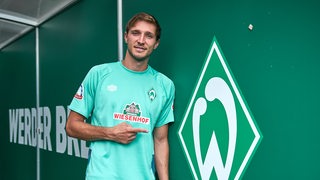 Niklas Stark posiert neben einem Werder-Logo im Weser-Stadion. 
