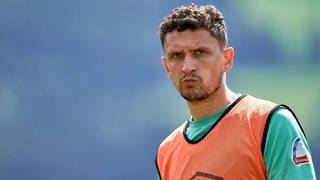 Werder-Verteidiger Milos Veljkovic schaut ernst während eines Trainings und trägt ein orangefarbenes Leibchen.