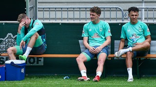 Die Werder-Spieler Marvin Ducksch, Jens Stage und Lee Buchanan sitzen auf einer Bank.