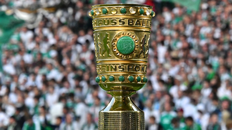 Nahaufnahme der Siegertrophäe im DFB-Pokal vor einer Tribüne mit Fans auf den Rängen.
