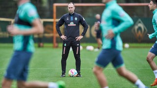 Werder-Trainer Ole Werner beobachtet ruhig das Treiben seiner Spieler beim Aufwärmen.