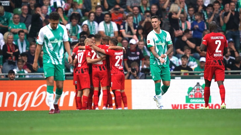 Werder-Spieler Marco Friedl und Milos Veljkovic schauen enttäuscht, während die Frankfurter Spieler hinter ihnen jubeln.