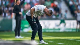 Werder-Trainer Ole Werner beugt sich an der Seitenlinie in einer Frustgeste weit nach vorne runter.