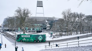 Blick auf das schneebedeckte Weserstadion, der grüne Werder-Mannschaftsbus fährt vor.
