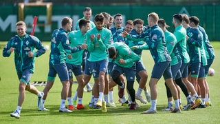 Werder-Spieler kabbeln und rangeln im Spaß lachend auf dem Trainingsplatz.