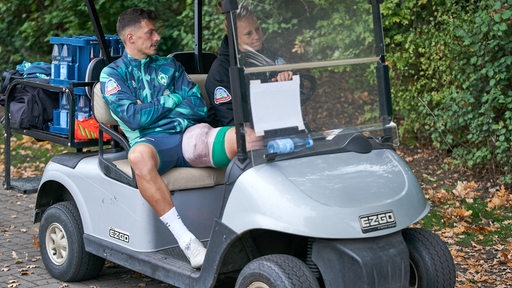 Werder-Spieler Nikolai Rapp wird mit dick bandagiertem Oberschenkel im Golfkart vom Trainingsplatz gefahren.