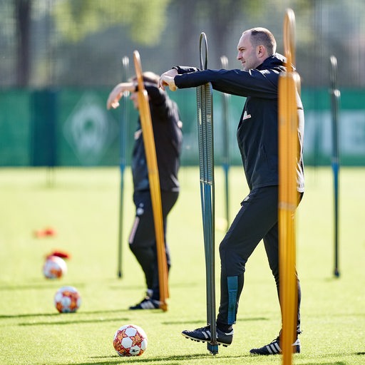 Werder-Coach Ole Werner lehnt sich beim Training auf eines der Metallmännchen und beobachtet seine Spieler.