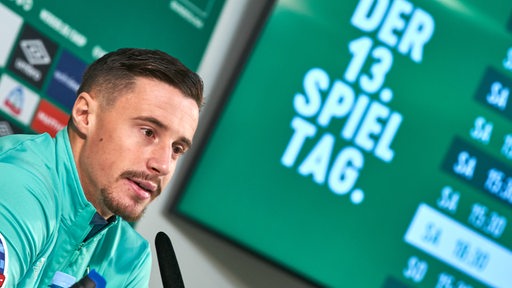 Werder-Kapitän Marco Friedl sitzt vor dem 13. Spieltag bei einer Pressekonferenz.