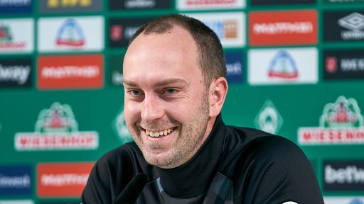 Werder-Trainer Ole Werner lächelt bei der Pressekonferenz.