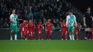 Fußballspieler in grün-weißen Trikots rechts und links verschwommen zu sehen wirken enttäuscht. Im Hintergrund Spieler in roten Trikots freuen sich.