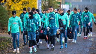 Werder-Spieler kommen als Gruppe den Weg entlang zum Trainingsplatz.