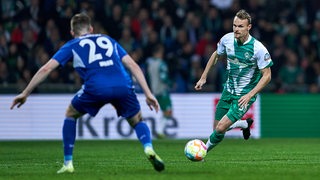Werder-Spieler Christian Groß dribbelt mit dem Ball auf seinen Schalker Gegenspieler zu.