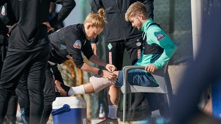 Werder-Spieler Romano Schmid wird am Rande des Traningsplatzes das linke Knie dick bandagiert.