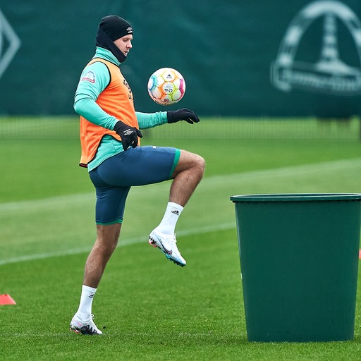 Werder-Stürmer Niclas Füllkrug spielt den Ball im Training mit dem Oberschenkel hoch, um ihn eine große Plastiktonne zu befördern.