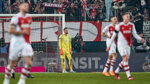 Werder-Keeper Jiri Pavlenka steht konsterniert am Torpfosten, während Kölner Spieler einen Treffer bejubeln.