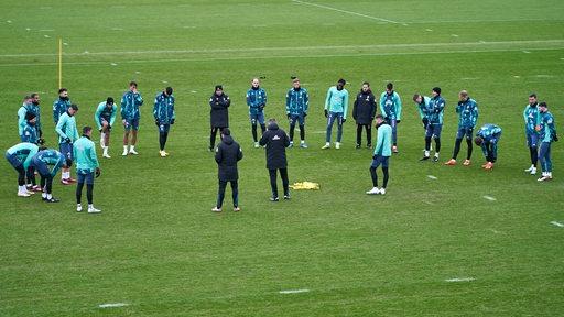 Blick aus der Ferne auf den Werder-Trainingsplatz, wo die Mannschaft Trainer Ole Werner umringt und ihm zuhört.