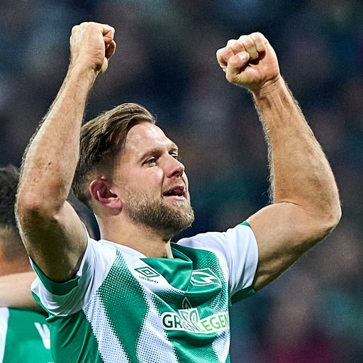 Werder-Stürmer Niclas Füllkrug reckt strahlend seine durchtrainierten Arme in die Höhe.