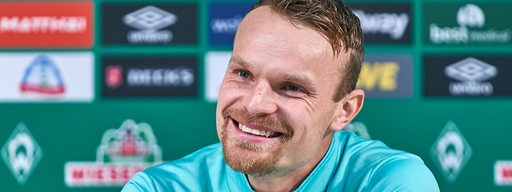 Werder-Spieler Christian Groß strahlt auf dem Podium einer Pressekonferenz.