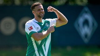 Werder-Stürmer Niclas Füllkrug spannt seinen linken Oberarm an und lacht.