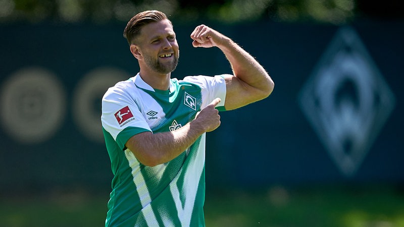 Werder-Stürmer Niclas Füllkrug spannt seinen linken Oberarm an und lacht.