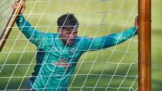 Werder-Stürmer Niclas Füllkrug stemmt sich am Rande des Trainings mit viel Kraft gegen das Tor, um es zur Seite zu schieben.