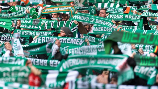Nahansicht auf die Bremer Ostkurve im Weser-Stadion, in der Fans dicht gedrängt ihre Werder-Schals hochhalten.