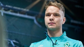 Werder-Profi Niklas Schmidt sitzt bei einem Interview vor einer Fototapete, die einen Blick ins Weser-Stadion zeigt.