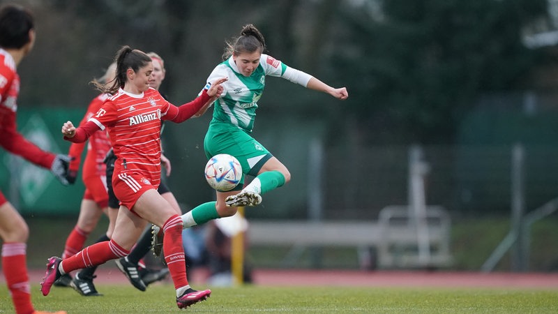 Eine Werder-Spielerin springt im Zweikampf mit einer Bayern-Spielerin hoch und nimmt den Ball im Sprung an.