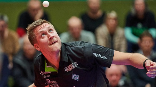 Werders Tischtennis-Spieler Mattias Falck schaut konzentriert hoch zum Ball in der Luft während des Aufschlags.