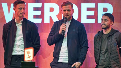Die Werder-Spieler Marco Friedl, Niclas Füllkrug und Leonardo Bittencourt stehen auf einer Bühne.
