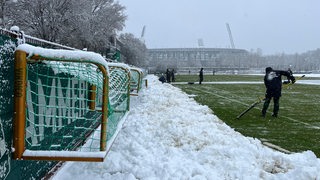 Arbeiter schippen den Schnee auf dem Trainingsplatz vor dem Weser-Stadion weg.