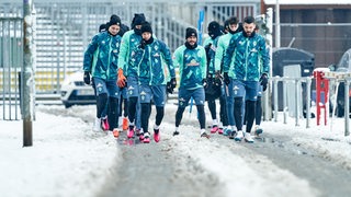 Werder-Spieler laufen den verschneiten Weg entlang zum Trainingsplatz vor dem Weser-Stadion.