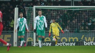 Werder-Torwart Jiri Pavlenka schlägt enttäuscht den Ball nach dem Treffer nach vorne, vor ihm frustrierte Mitspieler.