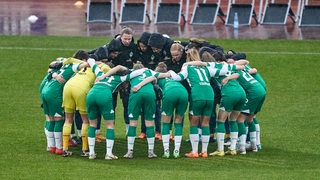 Werders Fußballerinnen stehen vor dem Spiel eng im Kreis zusammen, Arm in Arm.