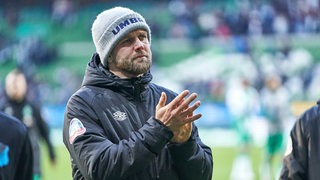 Werder-Stürmer Niclas Füllkrug applaudiert nach dem Spiel den Fans in dicker schwarzer Jacke und grauer Wollmütze auf dem Kopf.